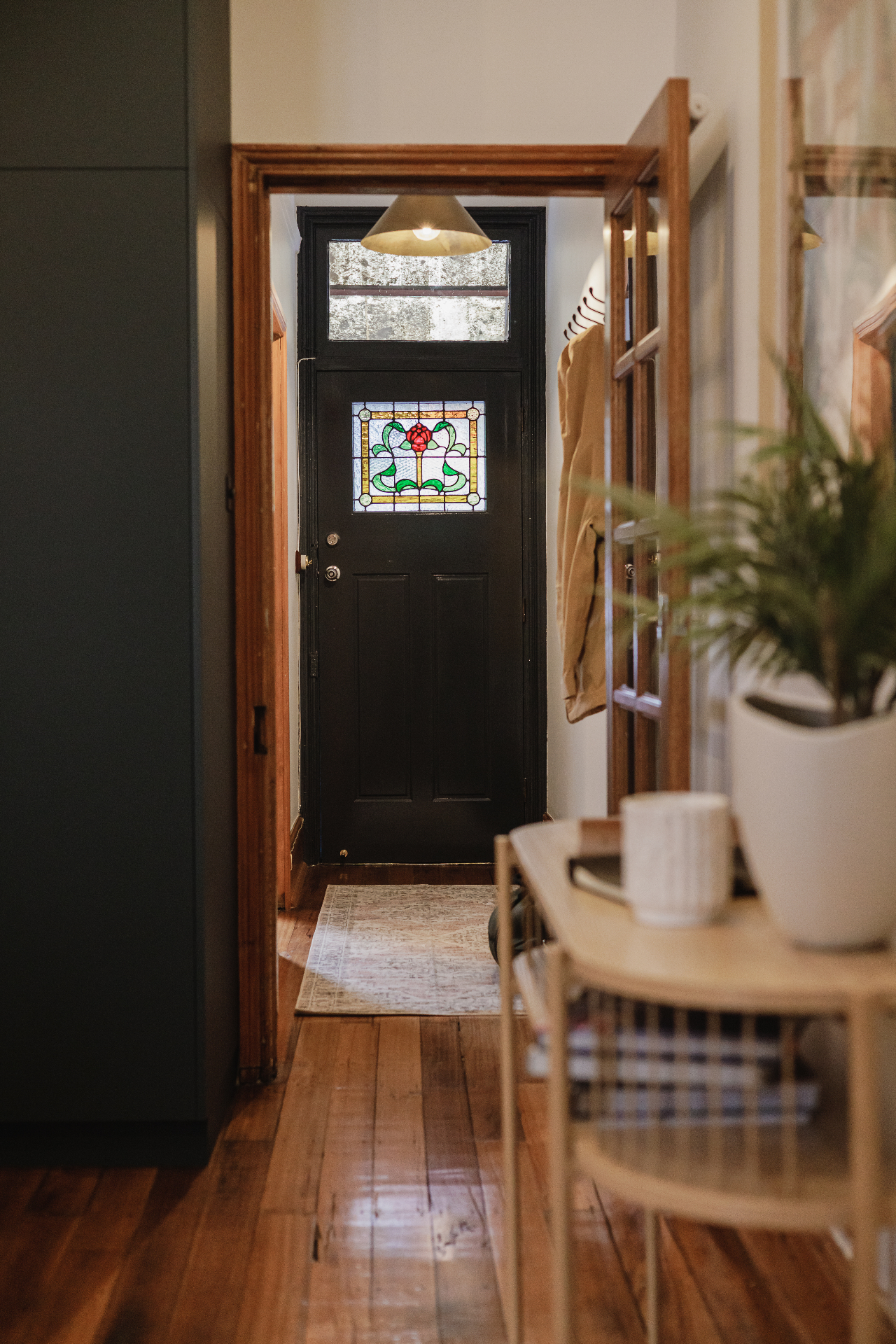 Black front door with stained glass and warm timber hallway at Hjemme Hobart